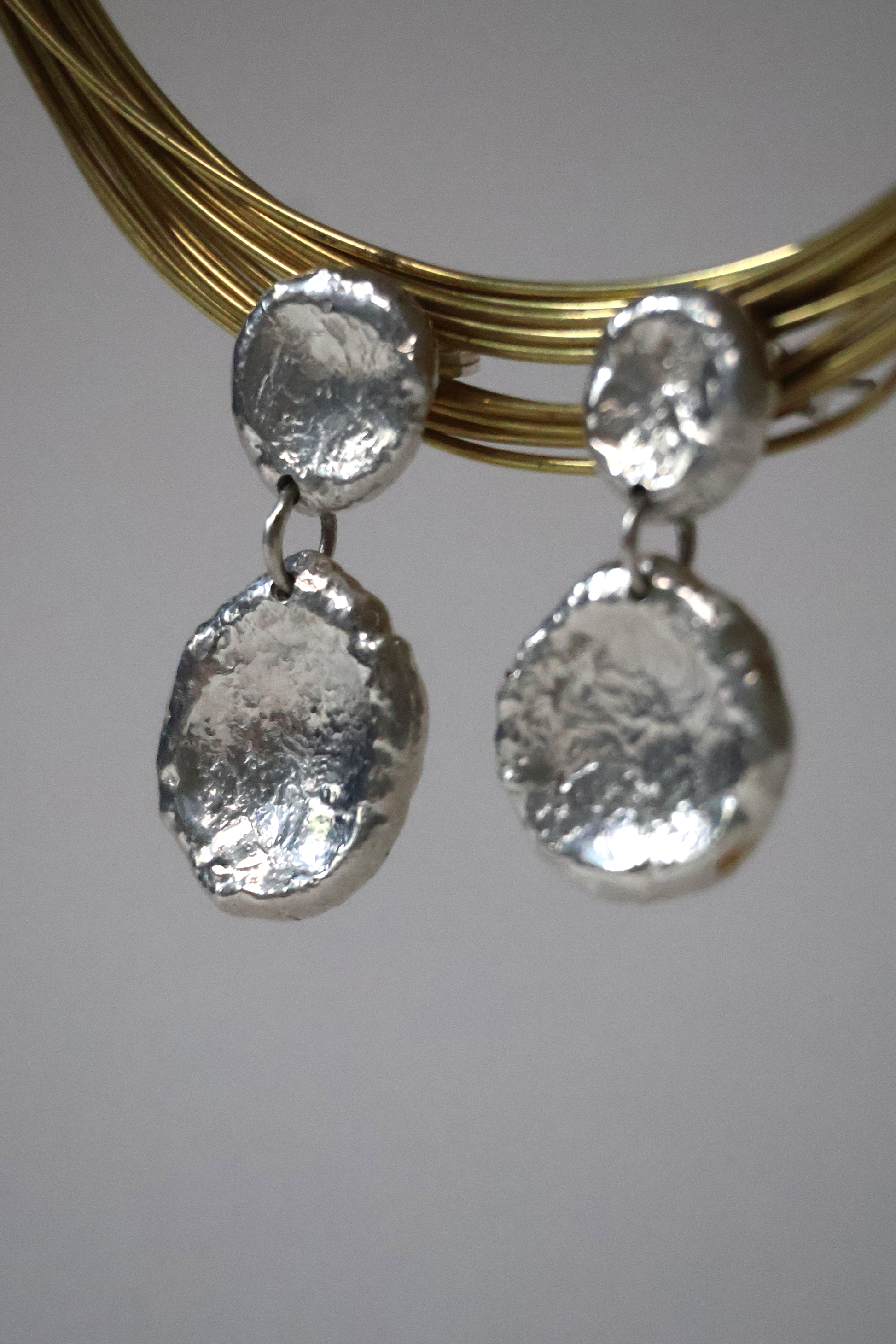 Silver earrings with textured round pendants on a gold wire against a white background