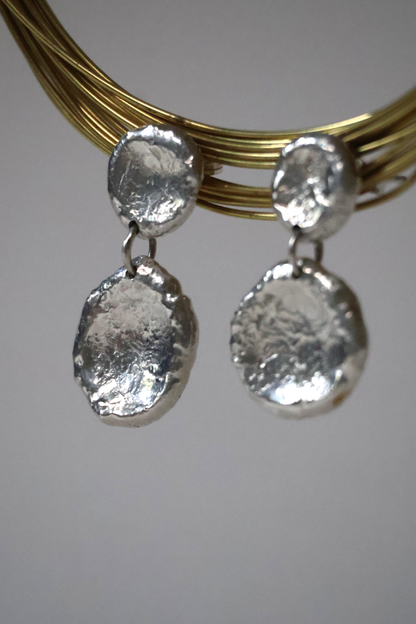 Silver earrings with textured round pendants on a gold wire against a white background